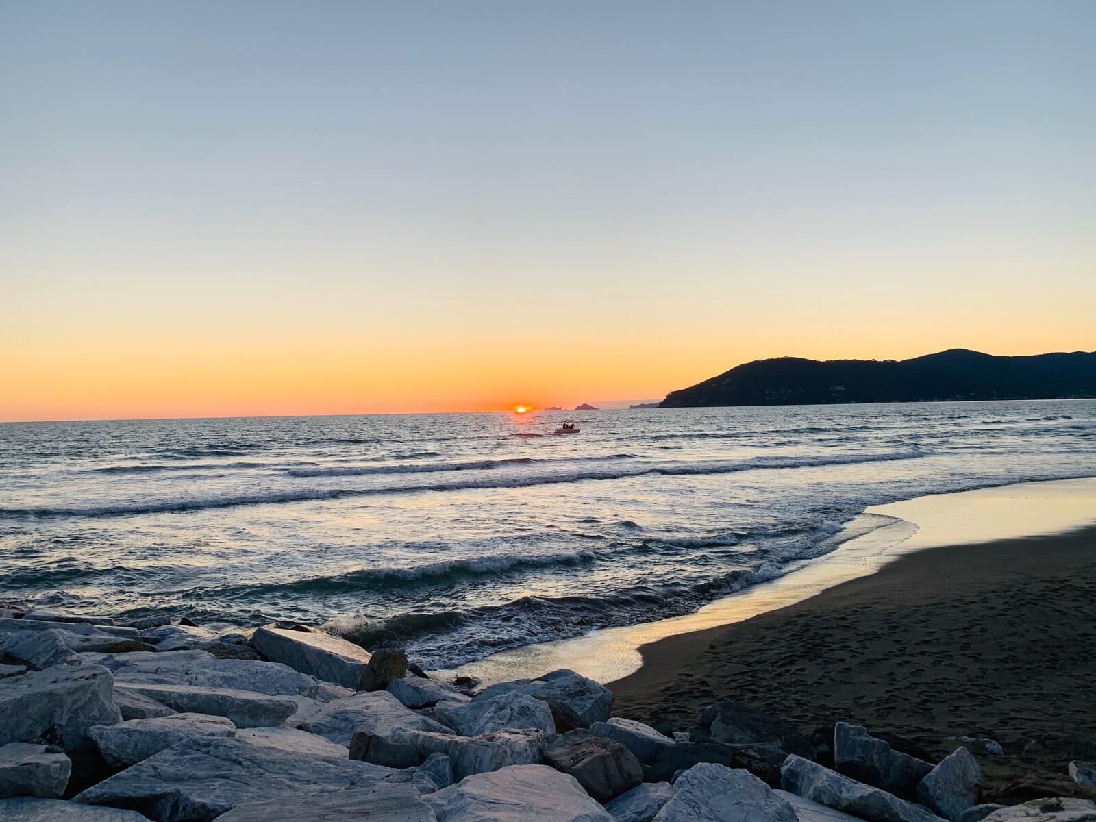 A beach with a rocky foreground and a sunset in the background.