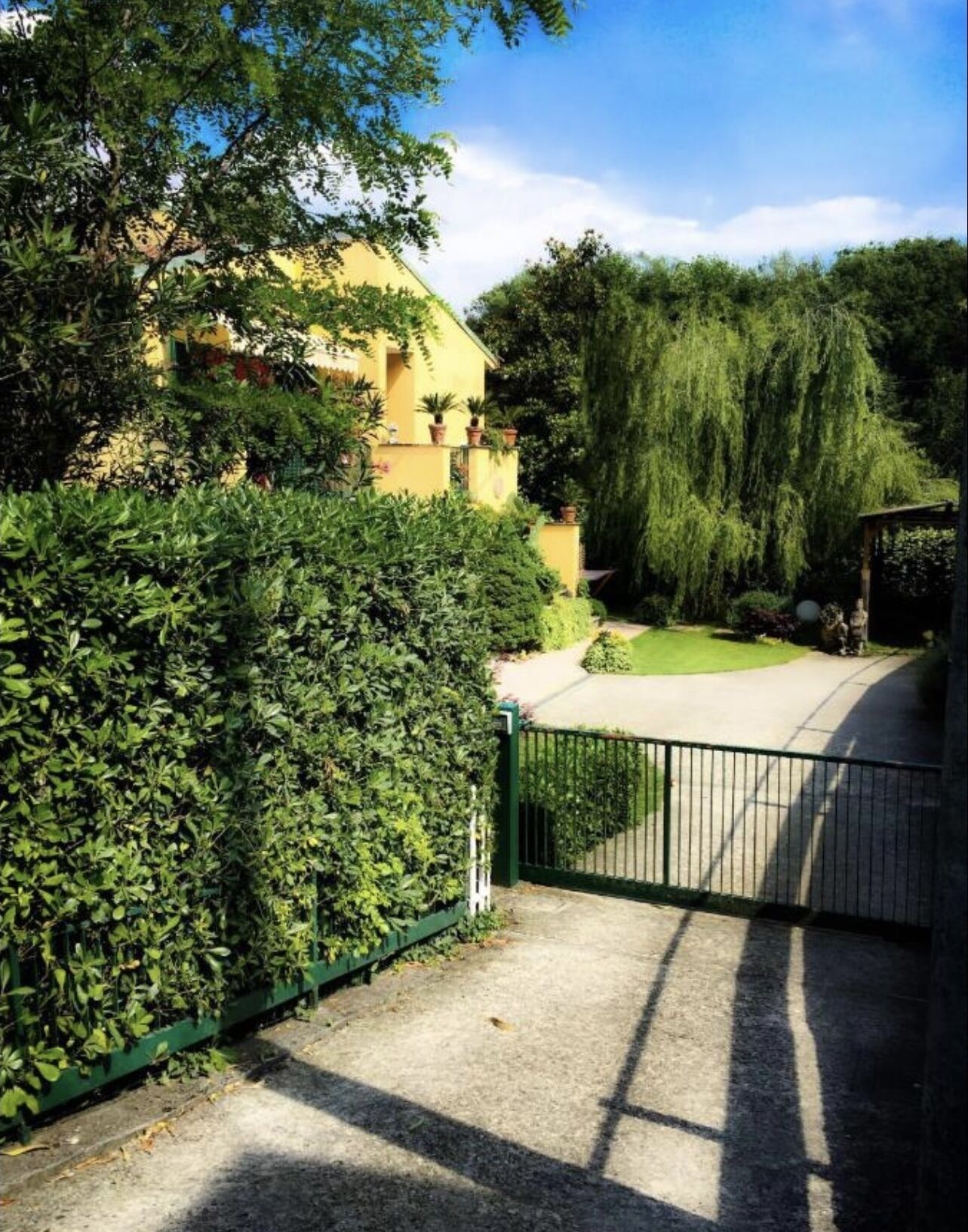 Una entrada con reja a una propiedad con jardín cuidado y un edificio al fondo.
