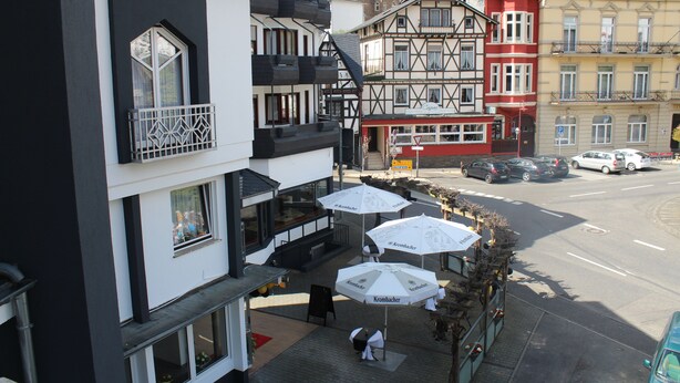 A hotel with a balcony, outdoor seating with umbrellas, and a view of the street. - Hotel Royal Santana (Altenahr)
