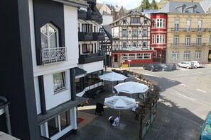 Een hotel met een balkon, zitplaatsen buiten met parasols en uitzicht op de straat.