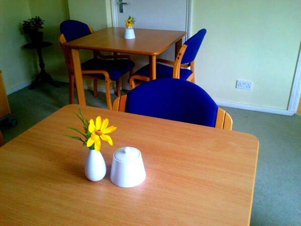 A room with a wooden table, two chairs, a small potted plant, and a vase with yellow flowers. - Malvern House (High Wycombe)
