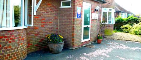 A brick building with a white-framed window, a signboard, and a potted plant.