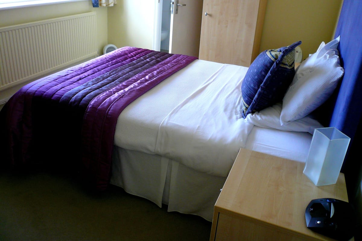 A bedroom with a bed, a bedside table, and a window.