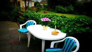 Ein weißer Tisch im Freien mit zwei Stühlen, einer davon mit einem blau-grün gestreiften Kissen.
