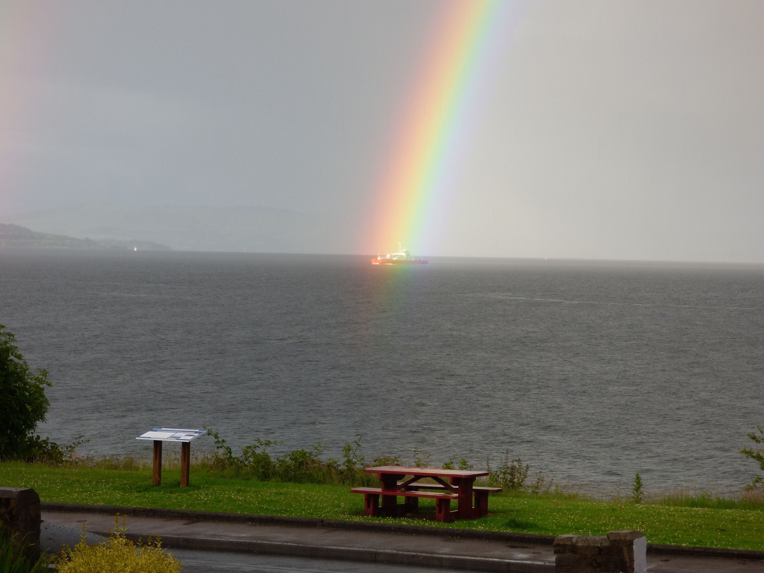 Une table de pique-nique près d’un plan d’eau, avec un arc-en-ciel en arrière-plan.