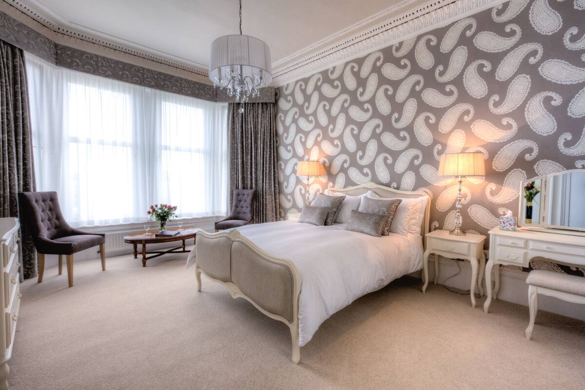 A spacious bedroom with a large bed, two bedside tables, a dresser, and a chair.