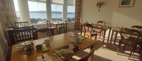 Comedor con vistas al mar, mobiliario de madera y una mesa dispuesta para dos.