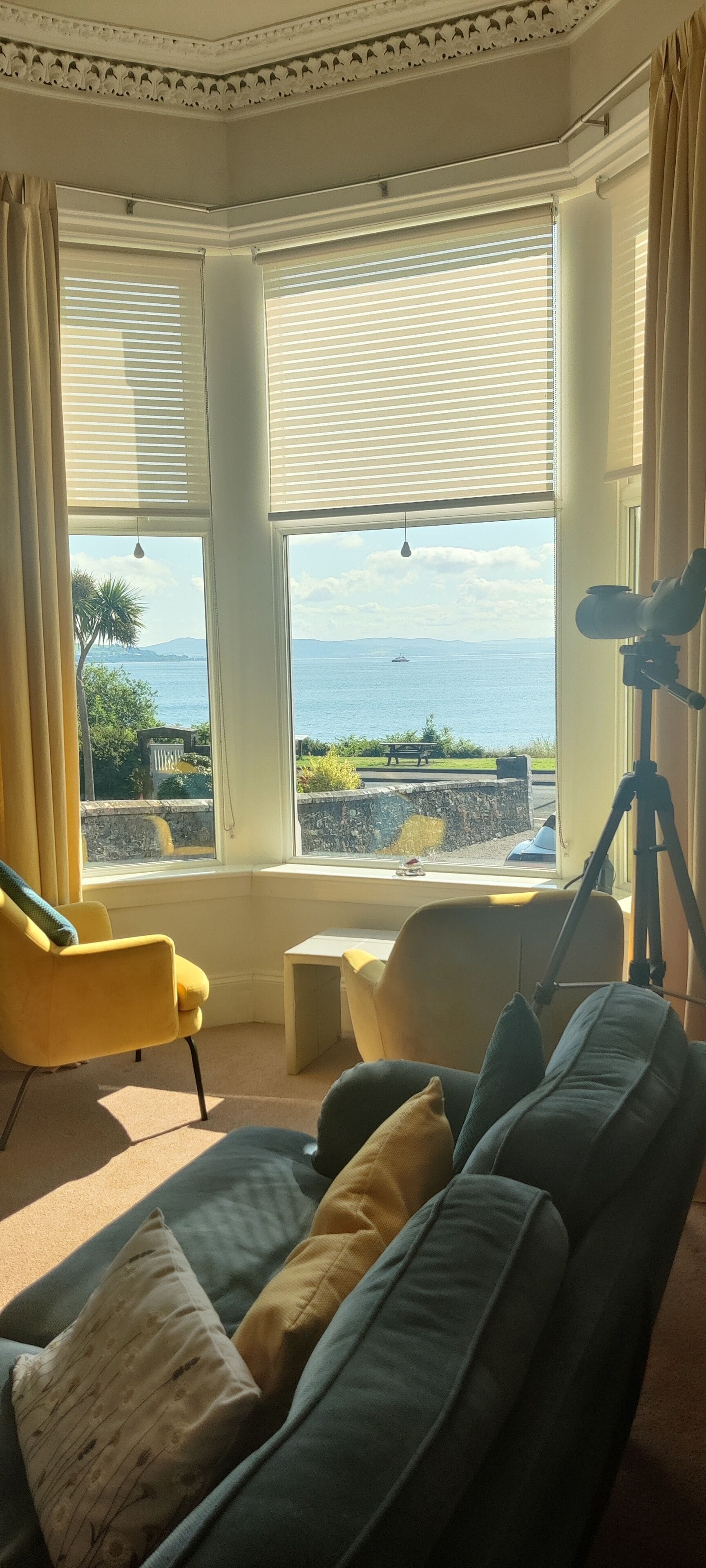Una habitación con un ventanal grande, un sofá, una silla y un telescopio.
