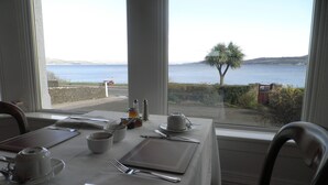 A dining table set with cutlery and a cup, overlooking a scenic view of the sea and hills. - Douglas Park Guest House (Dunoon)