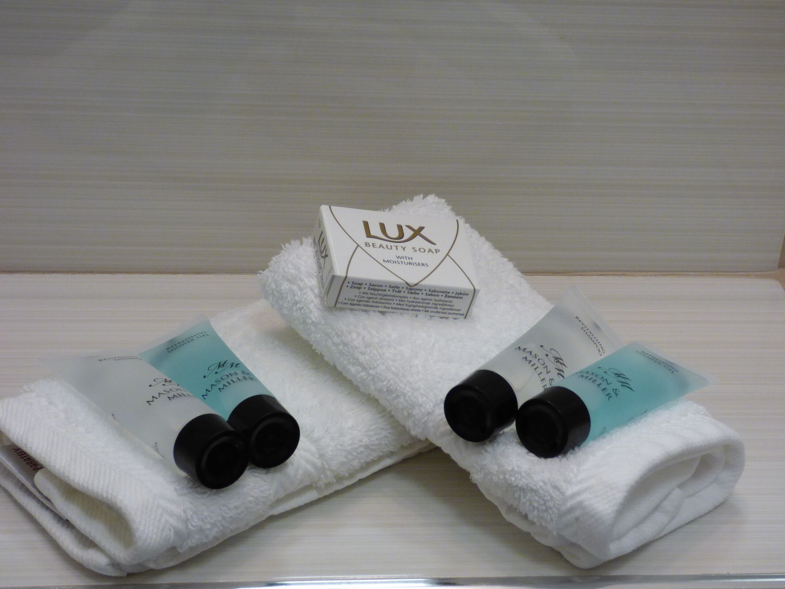 Una toalla blanca con botellas negras y una caja de jabón Lux Beauty sobre una superficie de madera.
