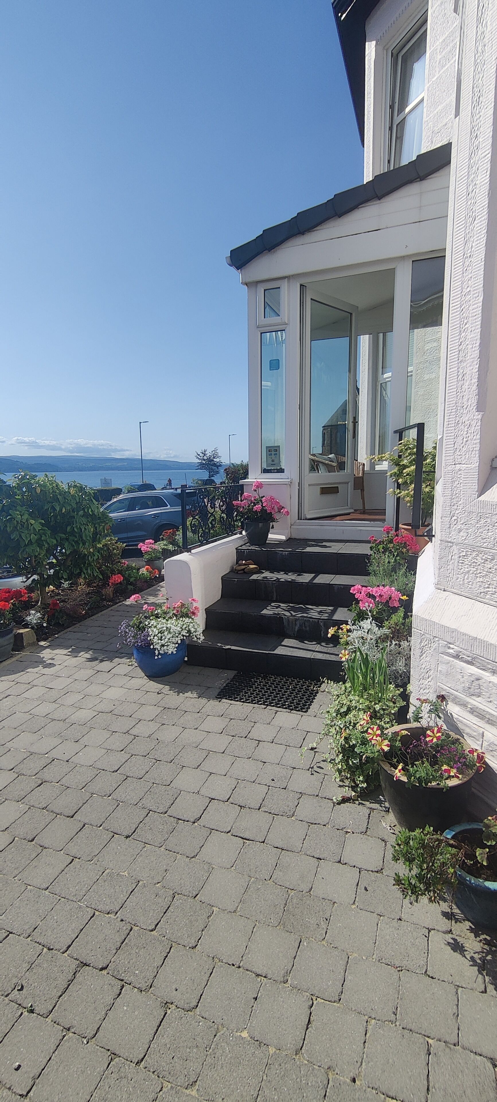 A house with a paved entrance, a small garden with flowers, and a view of the sea.