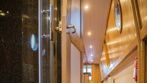 A corridor with wooden flooring, a glass shower enclosure, and a wooden wall with a circular mirror.
