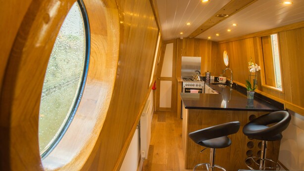 A wooden interior with a kitchen area, including a stove, sink, and bar stools.
