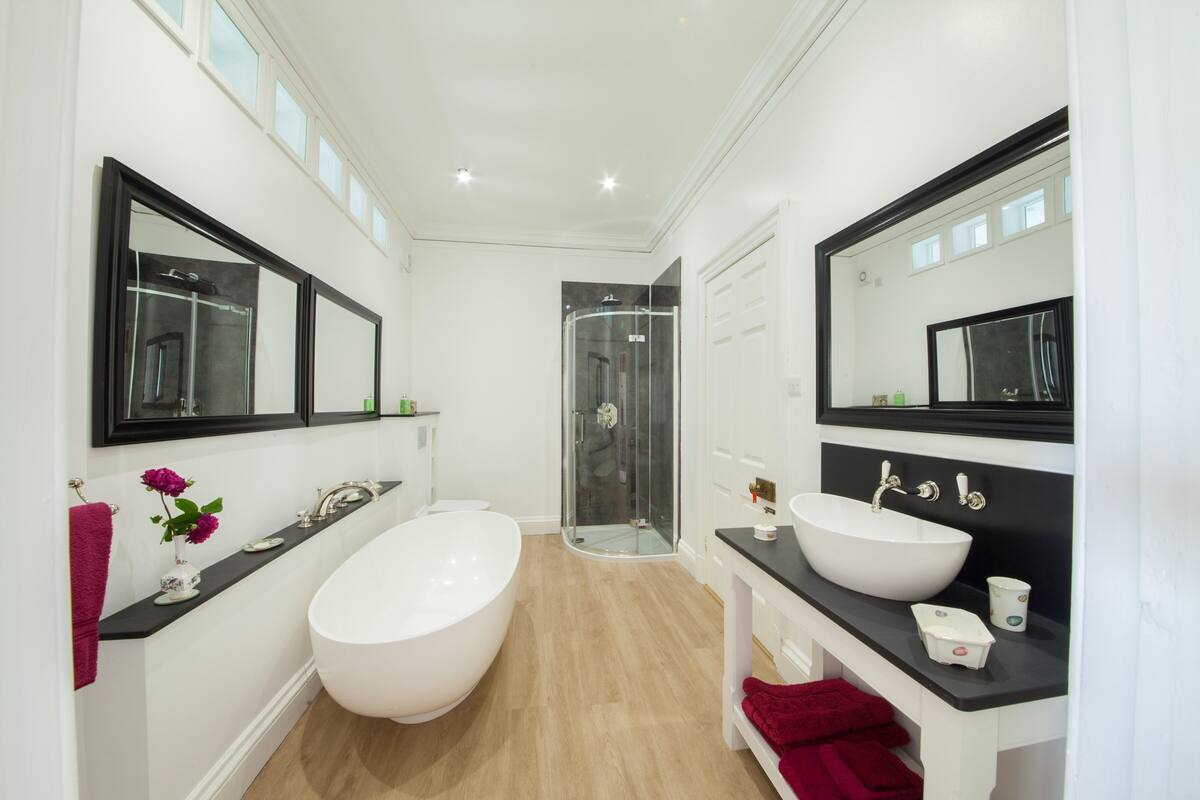 A modern bathroom with a large white bathtub, two sinks, a glass shower enclosure, and a mirror above the sink.