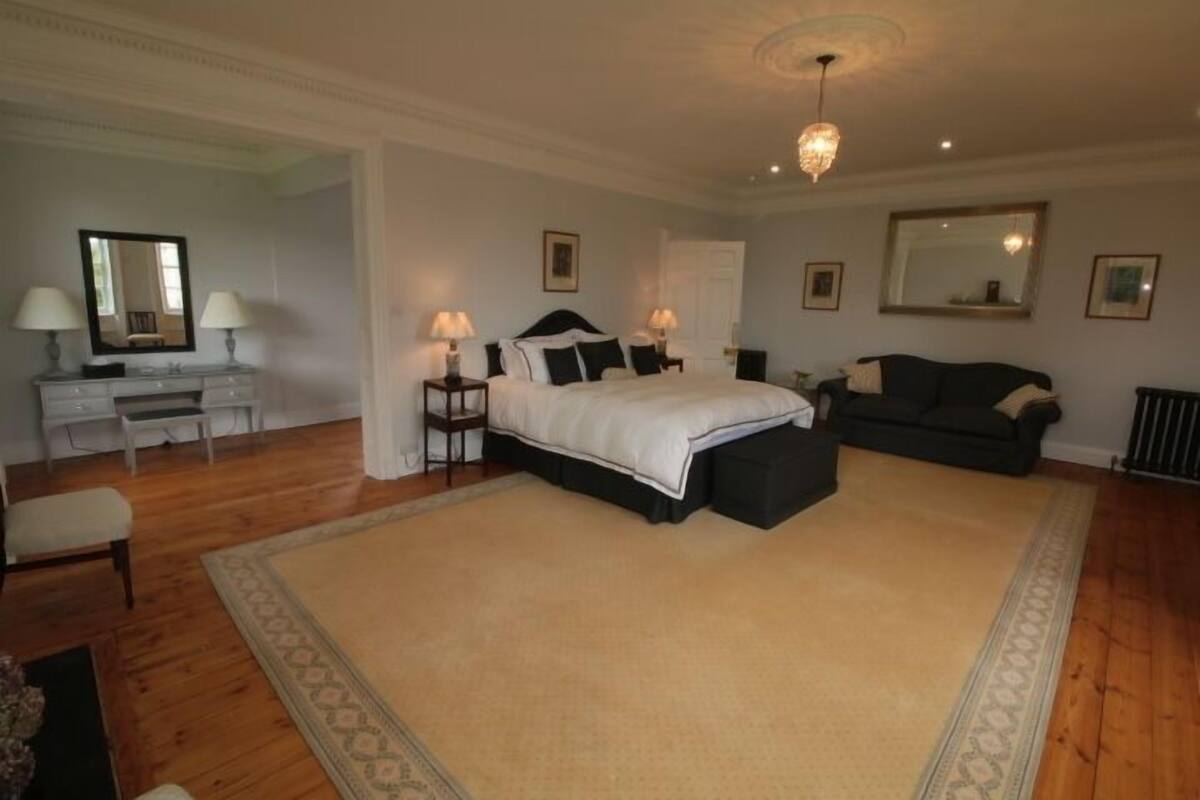 A spacious bedroom with a large bed, a dark sofa, and a white dresser.