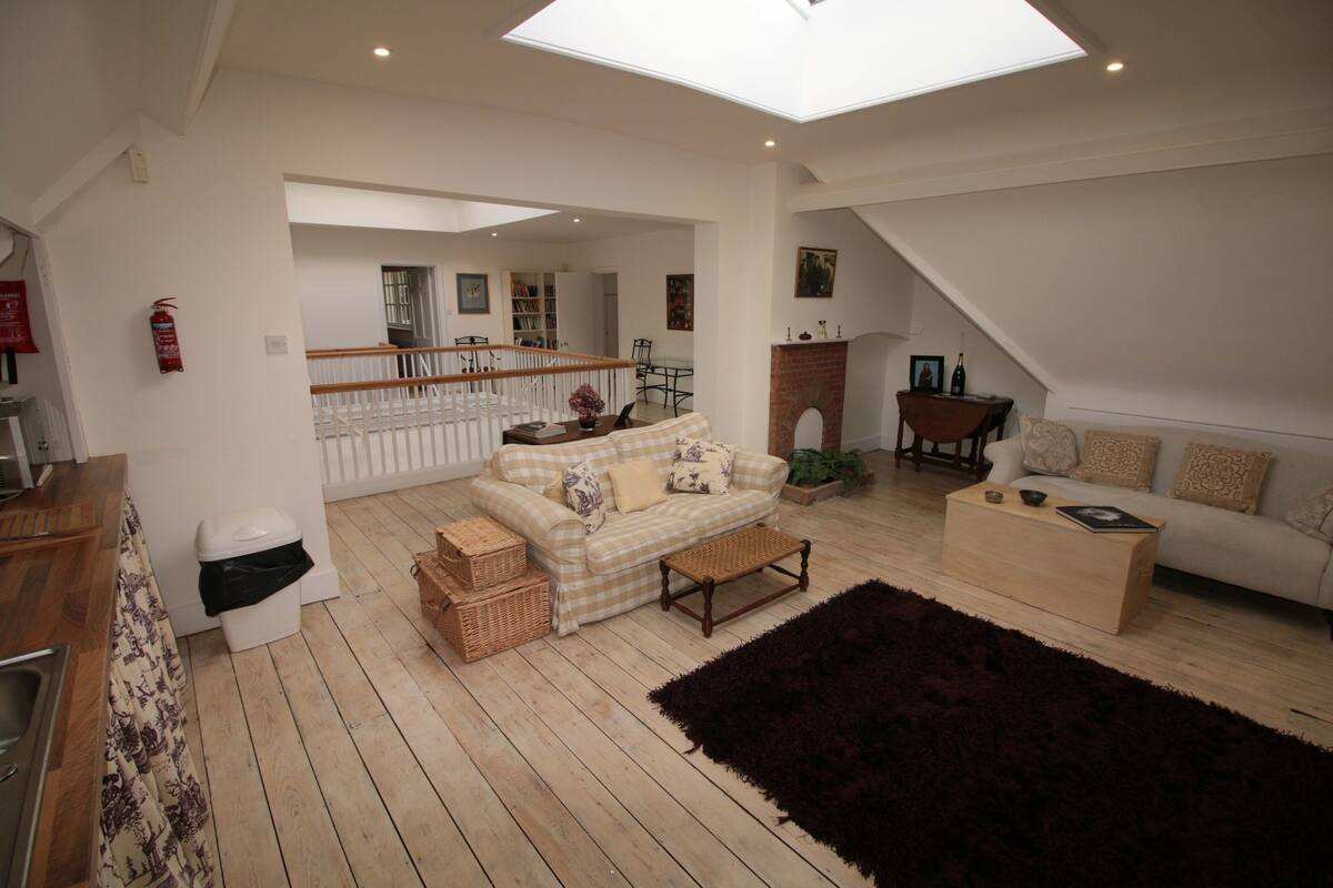 A spacious living area with a high ceiling and skylight, a cozy sofa set, a wooden coffee table, and a dark rug.