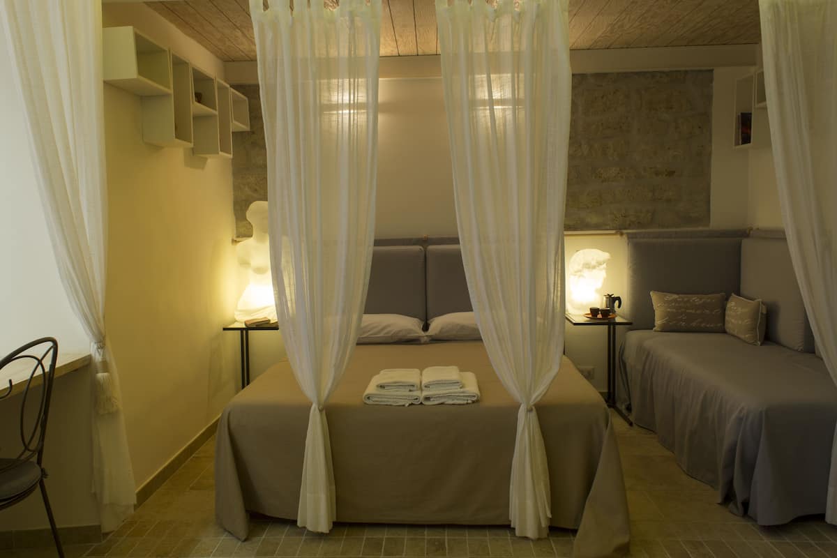 A hotel room with a large bed, two bedside tables with lamps, a chair, and a stone wall.
