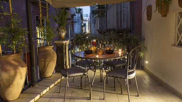 An outdoor patio with a round table and chairs, surrounded by large potted plants and a decorative wall. - Casa Latina B&B (Naples)