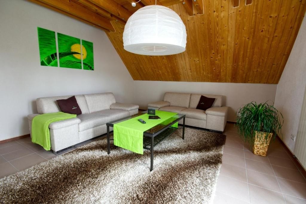 A modern living room with a high ceiling, a sofa set, a coffee table, and a hanging light fixture.