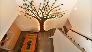 A modern interior with a unique tree-shaped light installation, a staircase, and a dining area with a wooden table and chairs.