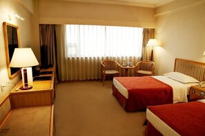 A hotel room with two beds, a desk, a chair, a TV, and a window with curtains. - Media Center Hotel - Beijing (BEIJING)