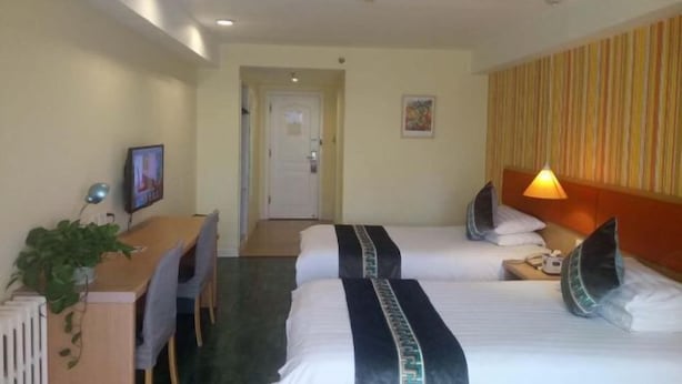 Une chambre d’hôtel avec deux lits, un bureau avec une chaise, une lampe et une plante.