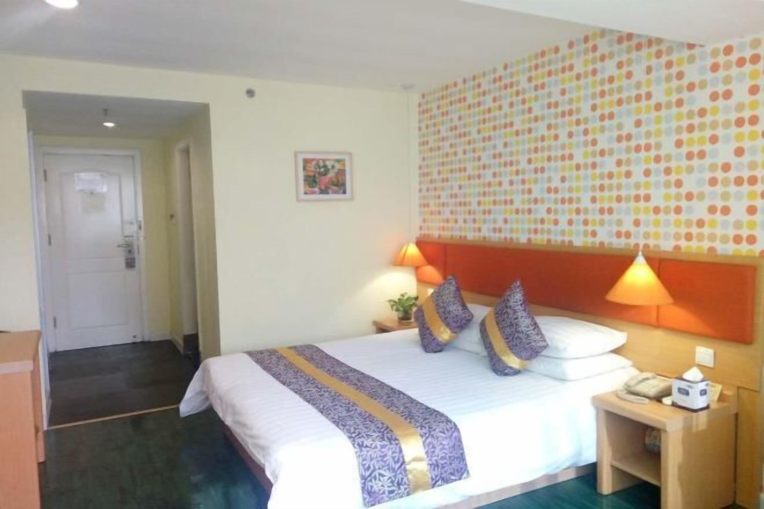A hotel room with a bed, two bedside lamps, a nightstand, and a patterned wall.