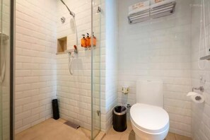A bathroom with white tiled walls, a glass shower enclosure, a white toilet, and a trash bin. - Orange Hotel (Ningbo)