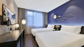 Habitación de hotel con dos camas, un escritorio con computadora, televisor y un amplio ventanal con cortinas.
