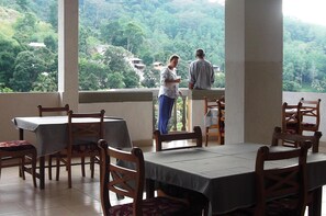 A dining area with tables and chairs, a balcony with a view of a lush green landscape. - Majestic Tourist Hotel (Kandy)