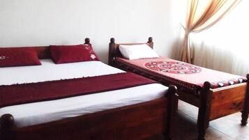 A double bed with red and white bedding, a single bed with a patterned red cover, and a wooden headboard.
