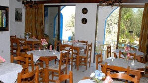 A dining area with multiple tables and chairs, some with tablecloths and flower arrangements. - Anthoula Sun (Rhodes)