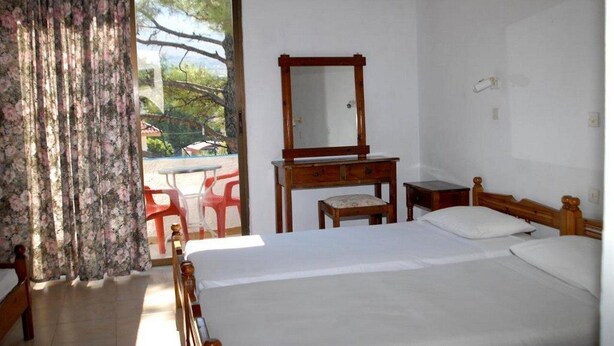 A bedroom with a bed, a wooden dresser, a mirror, and a window with curtains. - Anthoula Sun (Rhodes)