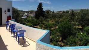 A terrace with blue plastic chairs and a table, overlooking a landscape with trees and buildings. - Anthoula Sun (Rhodes)