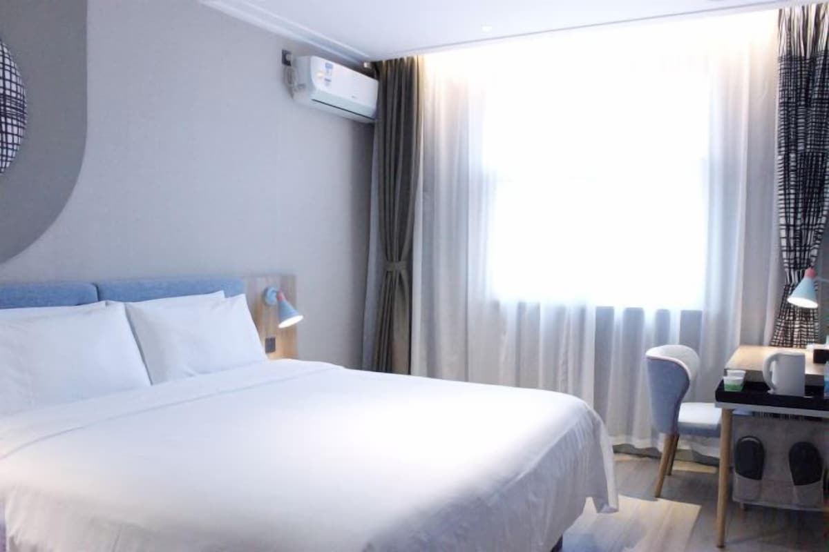 Ein Hotelzimmer mit Bett, Schreibtisch, Stuhl und einem Fenster mit Vorhängen.