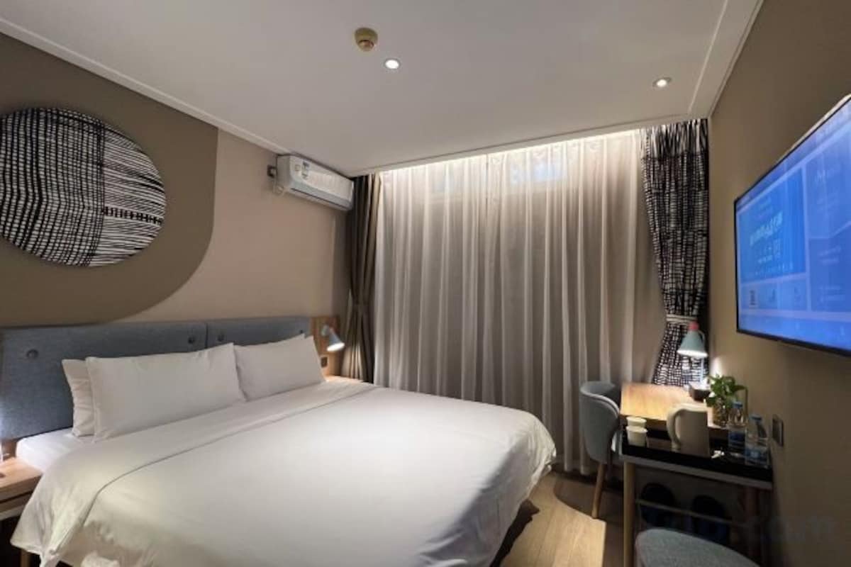 A hotel room with a bed, a desk, a chair, a TV, and curtains.