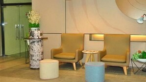 Eine Lobby mit zwei Sesseln, einem мраморный Beistelltisch, einem kleinen runden Tisch und einem blauen Hocker.