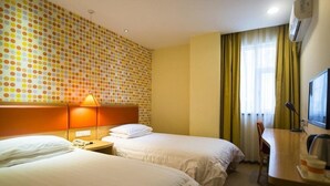 Ein Hotelzimmer mit zwei Betten, einem Schreibtisch, einem Stuhl, einer Lampe und einem Fernseher.