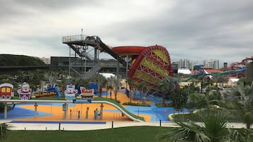 Entrada a un parque temático con una montaña rusa, una noria gigante y señalización colorida.