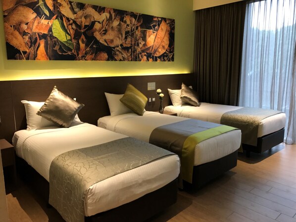 Una habitación de hotel con tres camas, un cuadro abstracto grande en la pared y una ventana con cortinas.