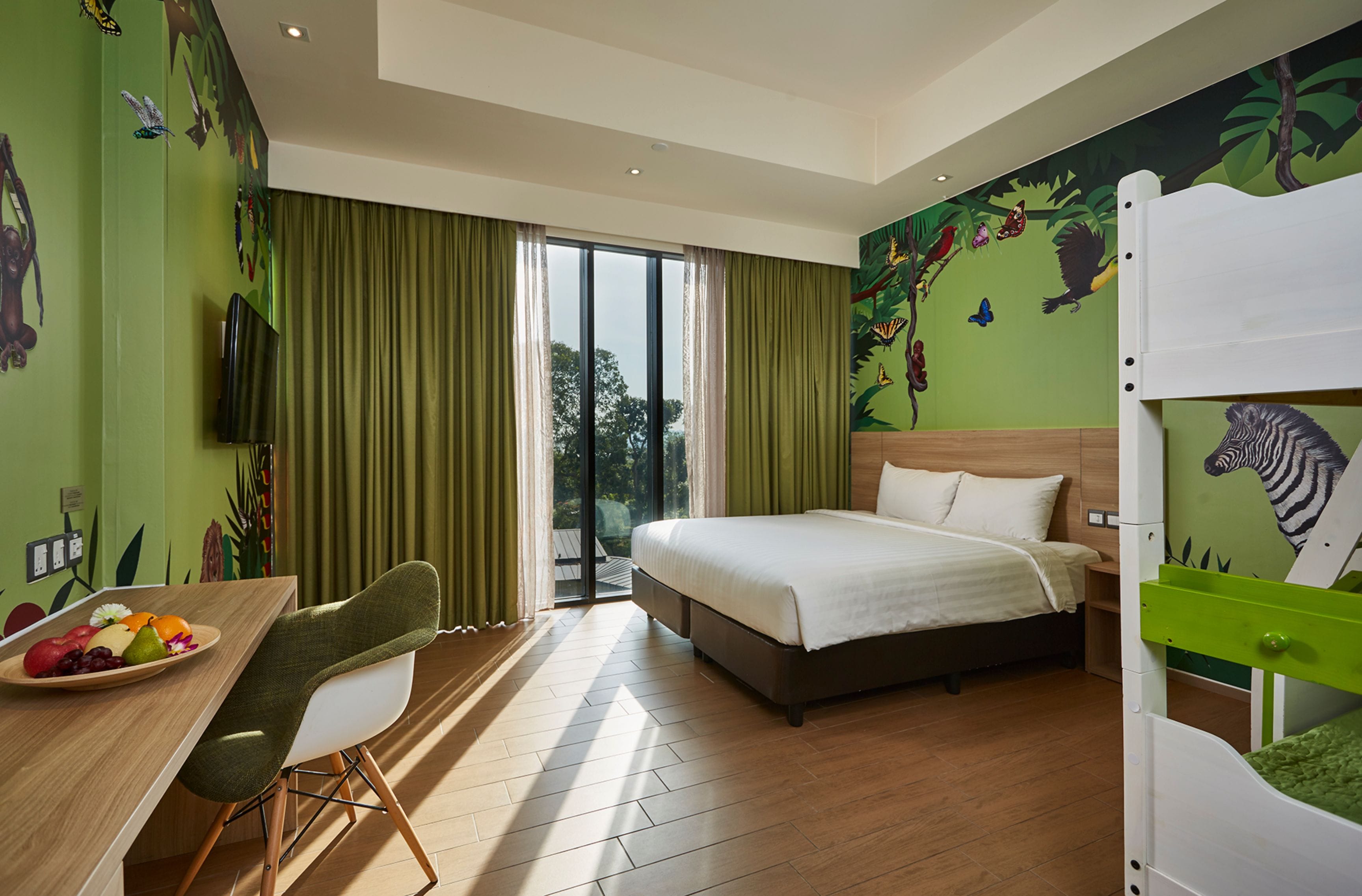 Quarto de hotel com cama, mesa de refeições com frutas, televisão e um mural de animais.