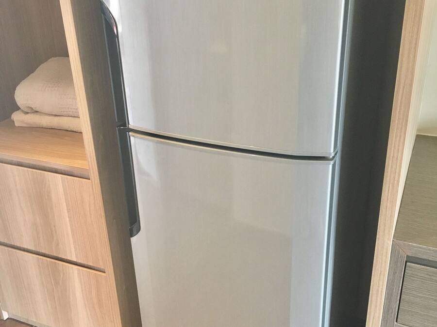 Un refrigerador compacto de acero inoxidable, con diseño de dos puertas, ubicado en una cocina moderna con alacenas de madera y piso de baldosas.