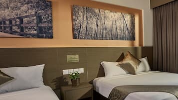 A hotel room with two beds, a nightstand with a plant, and two framed pictures on the wall.