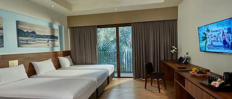 A hotel room with two beds, a desk with a computer, a TV, and a view of trees through the window.