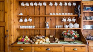 Un aparador de madera con estantes que exhiben tazas de té blancas y una variedad de productos horneados.