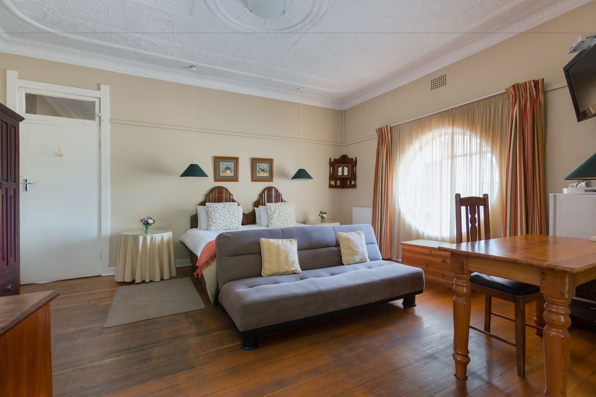 A bedroom with a bed, a sofa, a wooden desk, and a television.