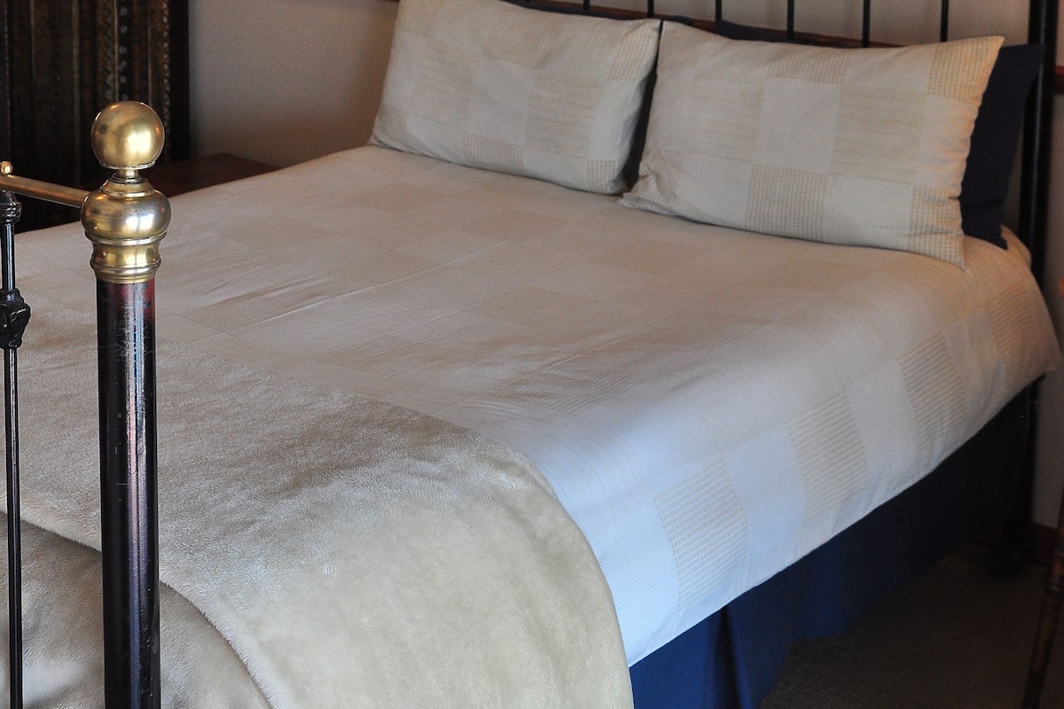 A neatly made bed with a headboard, a wall-mounted lamp, and a framed artwork above it.