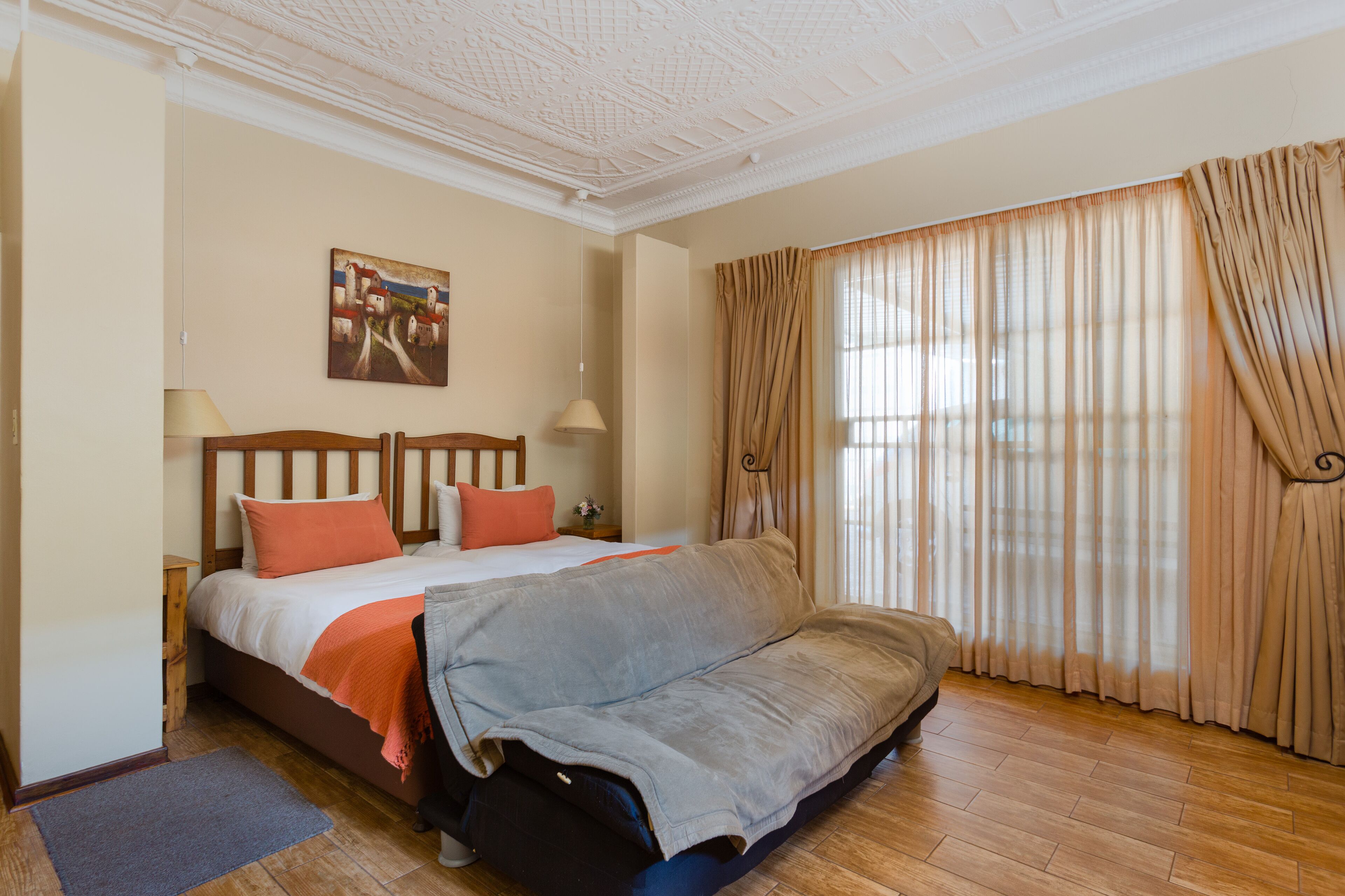 A hotel room with a bed, a sofa, a painting on the wall, and curtains on the window.