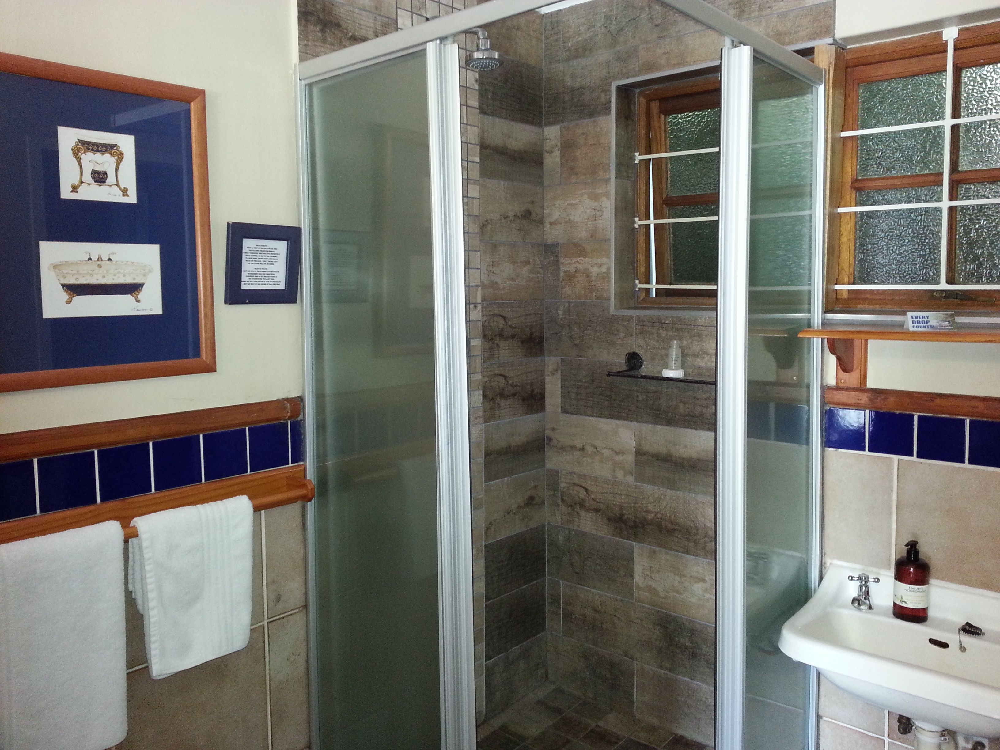 A bathroom with a glass-enclosed shower, a sink with toiletries, and framed pictures on the wall.