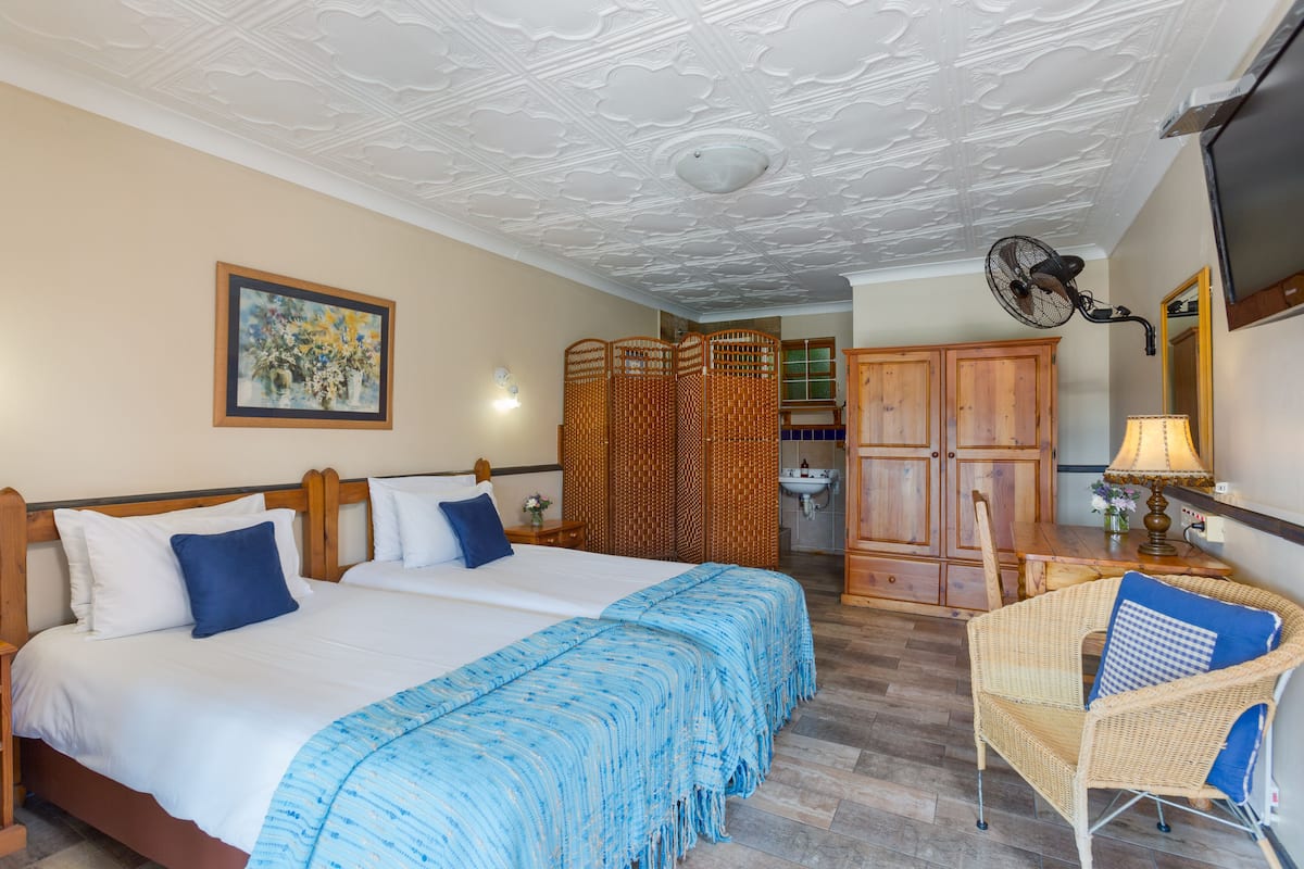 A hotel room with a large bed, a wicker chair, a wooden cabinet, and a ceiling fan.
